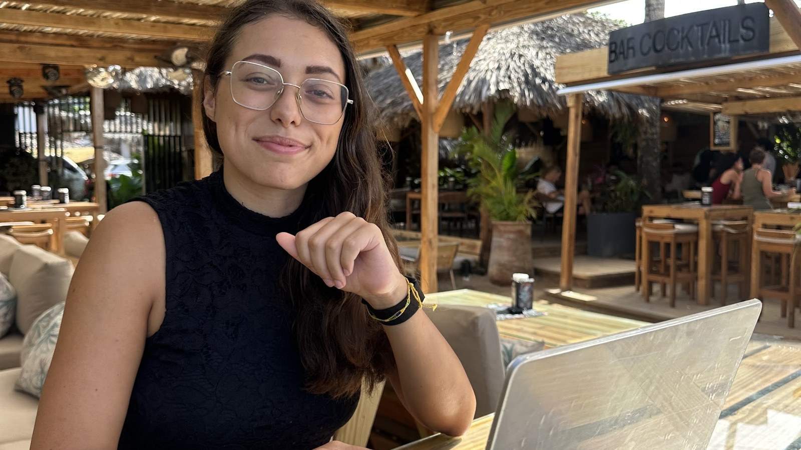 Clara lächelt am Laptop unter Bambusdach in einer Strandbar